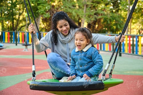 Preview: Happy Latin mother playing with her son on a swing in a park.