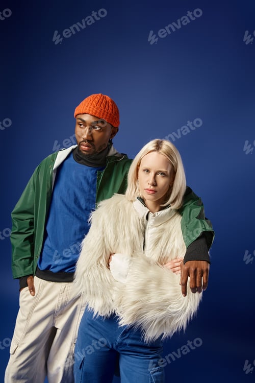 Preview: african american man hugging young woman in winter attire, diverse couple on blue backdrop