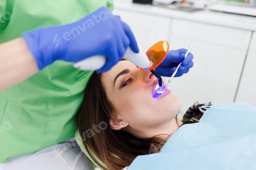 Preview: Girl treats teeth at the dentistry. Dentist using dental curing UV lamp on teeth of patient
