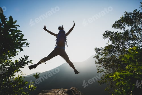 Preview: Hiker jumping on sunrise mountain top cliff edge