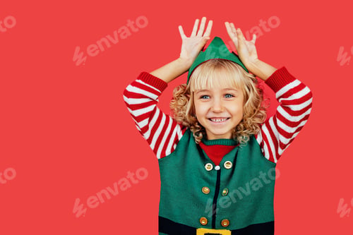 Preview: Little girl in Santa elf helper costume on bright red vivid color background.