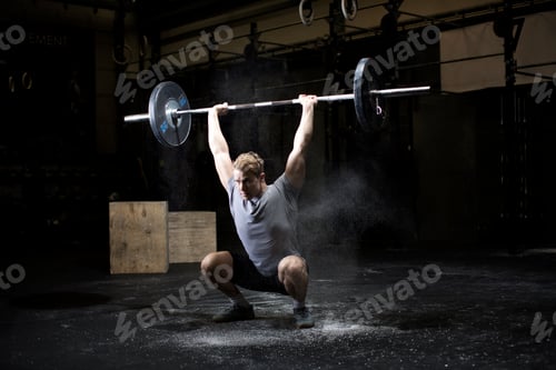 Preview: Young man weightlifting barbell in dark gym