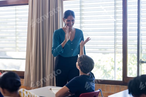 Preview: In school, Indian female teacher giving high-five to student in classroom, smiling and interacting