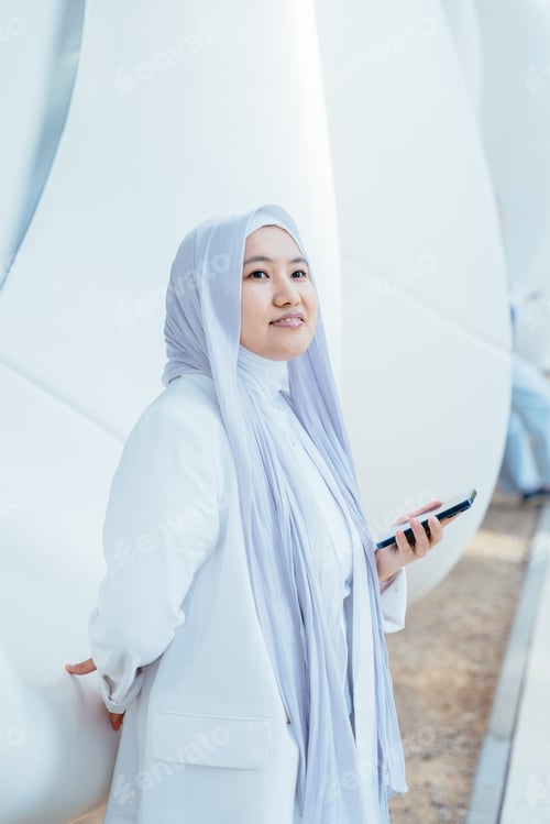 Preview: Muslim woman in white hijab smiling with smartphone in hand