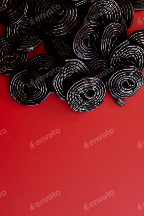 Preview: Flat lay tasty black liquorice candies on red background