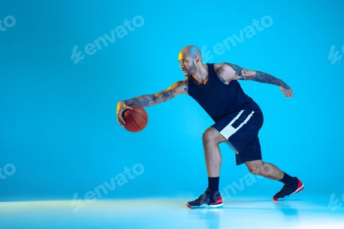 Preview: Young basketball player training isolated on blue studio background in neon light