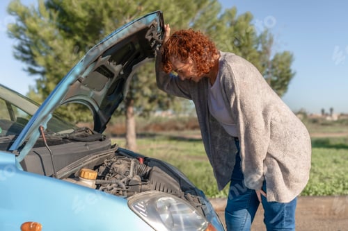 Preview: Woman looking at car engine with open hood having car trouble