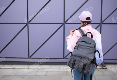 Preview: Rear view of a woman with a backpack against a wall background