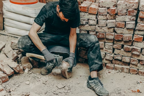 Preview: A young construction worker cleans bricks using an axe.