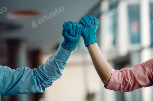 Preview: Close-up of colleagues fist bumping while wearing protective gloves.