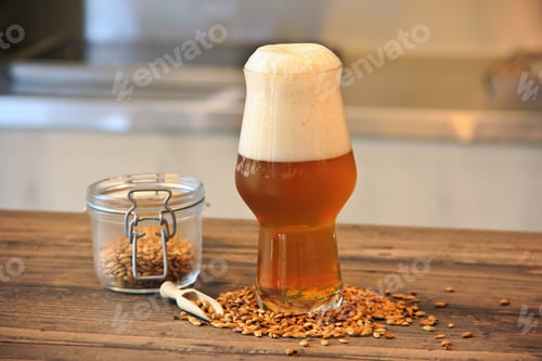 Preview: Horizontal shot of a glass full of Belgian wheat beer next to a container full of wheat seeds