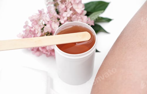 Preview: sugaring paste and spatula next to female leg. flowers on a background. depilation at home