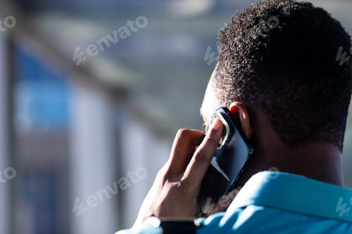 Preview: Rear view of african american businessman talking on smartphone in corridor at workplace