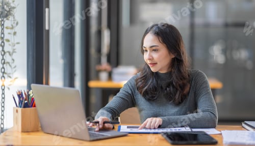 Preview: Freelancer Happy business Asian woman in knitwear taking notes at laptop sitting at desk office,