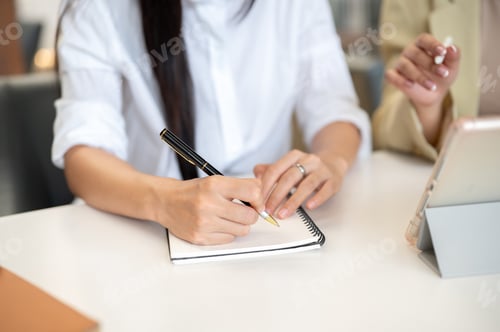 Preview: Close up of woman student's hand holding pen writing in notebook with teacher or supervisor talking.
