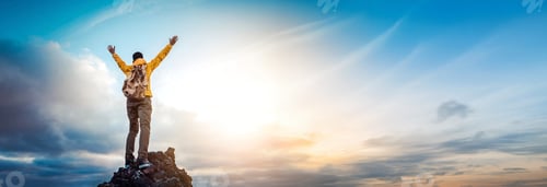 Preview: Man traveler on mountain summit enjoying nature view with hands raised over clouds