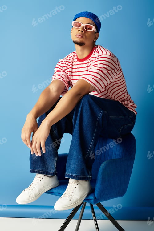 Preview: Young man showcases fashion with a beanie and striped shirt, seated casually on a chair