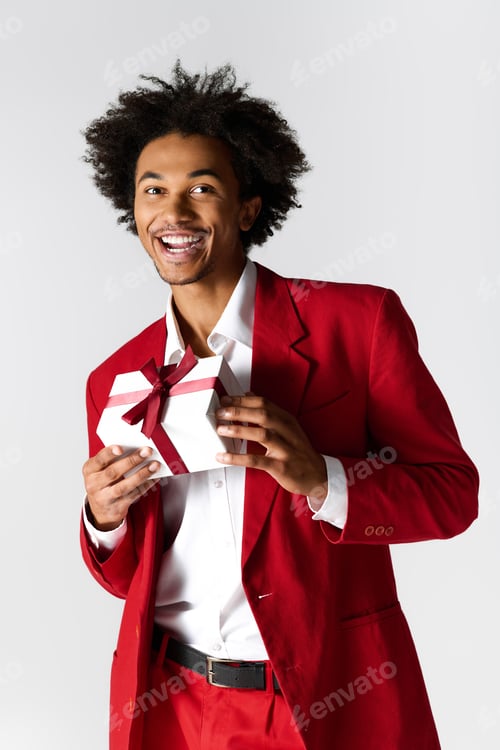 Preview: Handsome young man in elegant red attire joyfully presenting a beautifully wrapped gift