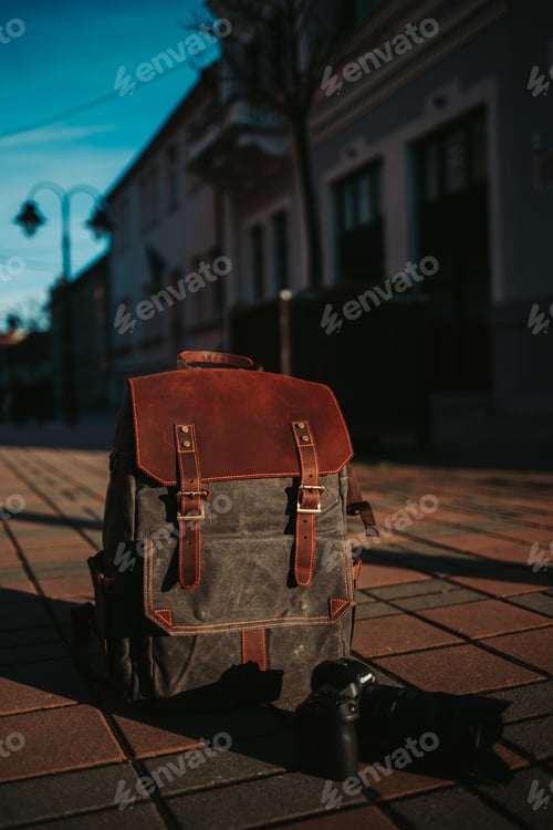 Preview: Vertical closeup shot of a grey and brown rucksack and a camera on the ground in the street