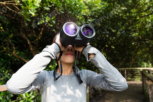 Preview: Woman looking though binoculars at jungle