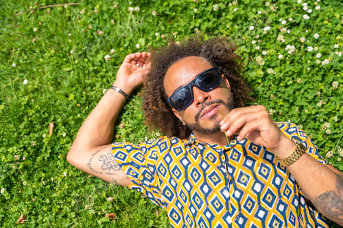 Preview: Afro hair man with sunglasses in summer enjoying a holiday or vacation day lying on the grass