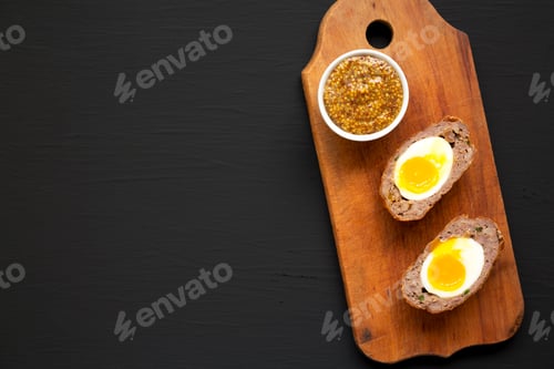 Preview: Homemade Scotch Eggs on a rustic wooden board on a black background, top view.