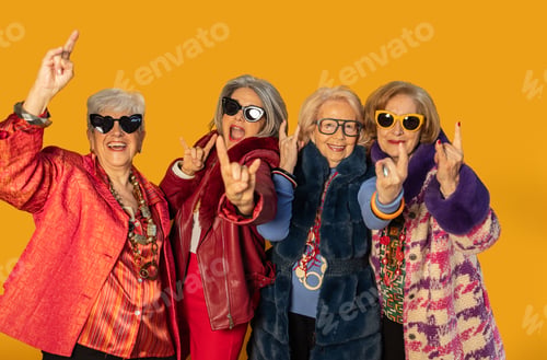 Preview: Group of stylish senior women showing rock and roll hand gesture on yellow background