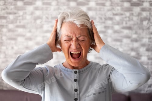 Preview: Desperate frustrated senior woman screaming in pain with hands on ears, standing at home alone