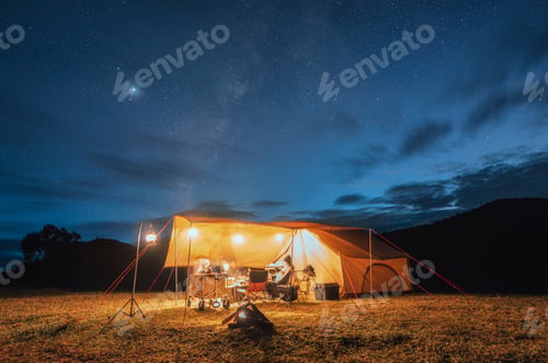 Preview: Tourists in yellow tent camping on hill with milky way in the night sky