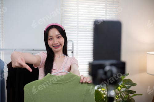 Preview: Woman asian online sell is using smartphone to while review shirt collection and talking with