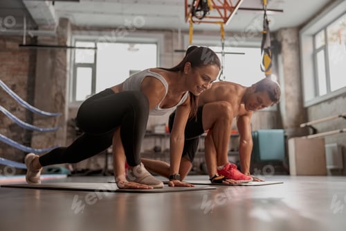 Preview: Attractive woman and man standing in plank in the gym, smiling