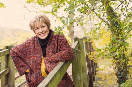 Preview: Mature woman leaning on wooden fence, smiling