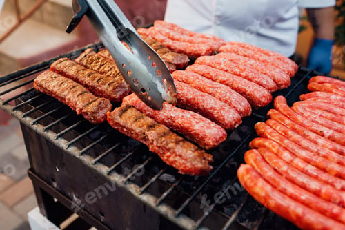 Vista previa: close up. Tasty sausages sizzling on a portable BBQ fire grilling on a summer picnic,