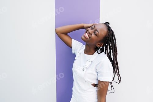 Preview: Happy woman with closed eyes wearing white clothes leaning on white wall with purple stripe