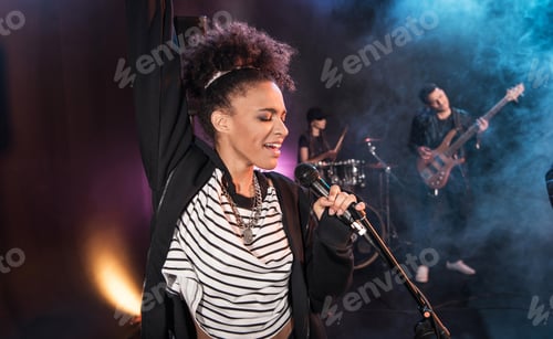 Preview: Female singer with microphone and rock and roll band performing hard rock music on stage