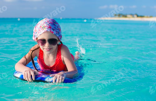 Preview: Little adorable girl on a surfboard in the turquoise sea