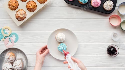 Preview: partial view of woman decorating cupcakes with icing bag on table with cupcake trays