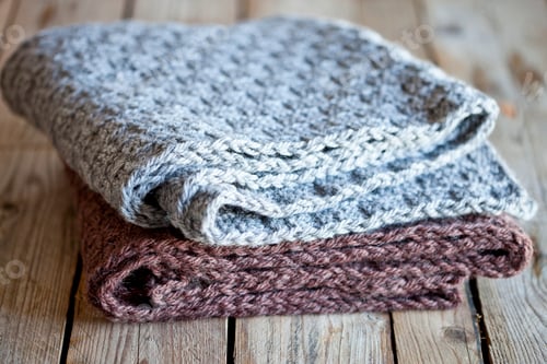 Preview: Close up of Stacked Knitted Blankets on Wood