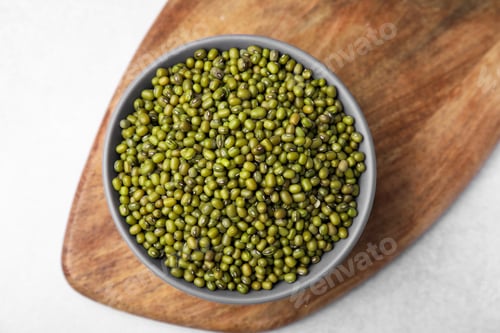 Preview: Bowl with green mung beans and wooden board on white table, top view
