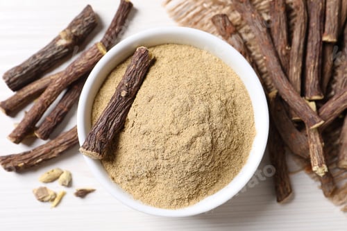 Preview: Powder in bowl and dried sticks of liquorice root on white table, flat lay