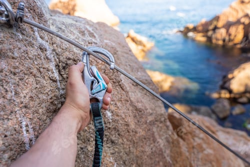 Preview: Climbing grips details young man's hand on rocks over the sea with rope and helmet.