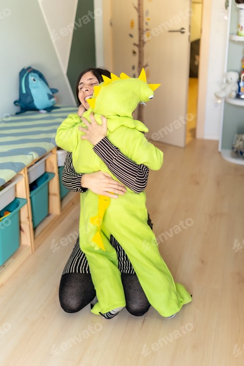 Preview: Mother hugging son wearing dinosaur costume in bedroom