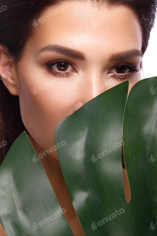 Vista previa: Hermosa mujer fresca con piel perfecta, maquillaje natural y hojas verdes. Un rostro de belleza.