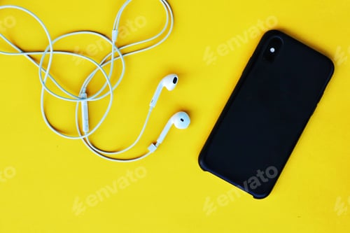 Preview: A flat lay of a black mobile phone and white earphones against a yellow background