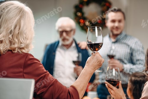 Preview: back view of woman making toast on christmas while celebrating with family