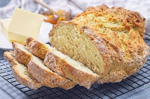 Preview: Freshly baked soda bread on cooling rack, sliced, butter and honey in the background, horizontal