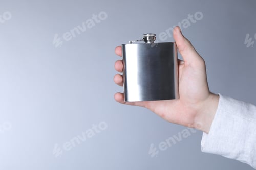 Preview: Man holding metal hip flask on light grey background, closeup. Space for text