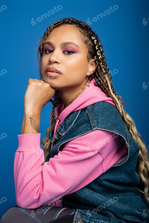Preview: portrait of african american woman with tattoo on hand looking at camera on blue background