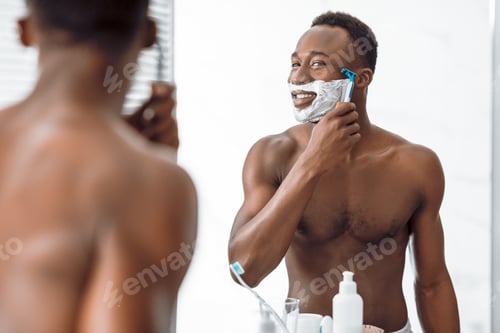 Preview: Shirtless African Man Shaving Face Covered With Foam In Bathroom