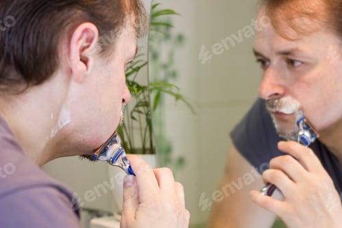 Preview: Closeup portrait of a Men shaving his face and looking at the mirror at the morning.